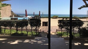 Vista da praia a partir de uma área coberta, com piscina, guarda-sóis e um deck de madeira.