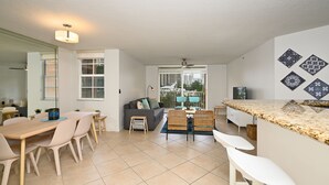 A modern kitchen with a large island, a dining area with a table and chairs, and a living area with a sofa and a coffee table.