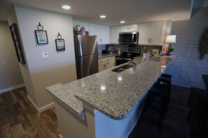 A modern kitchen with granite countertops, stainless steel appliances, and white cabinetry.