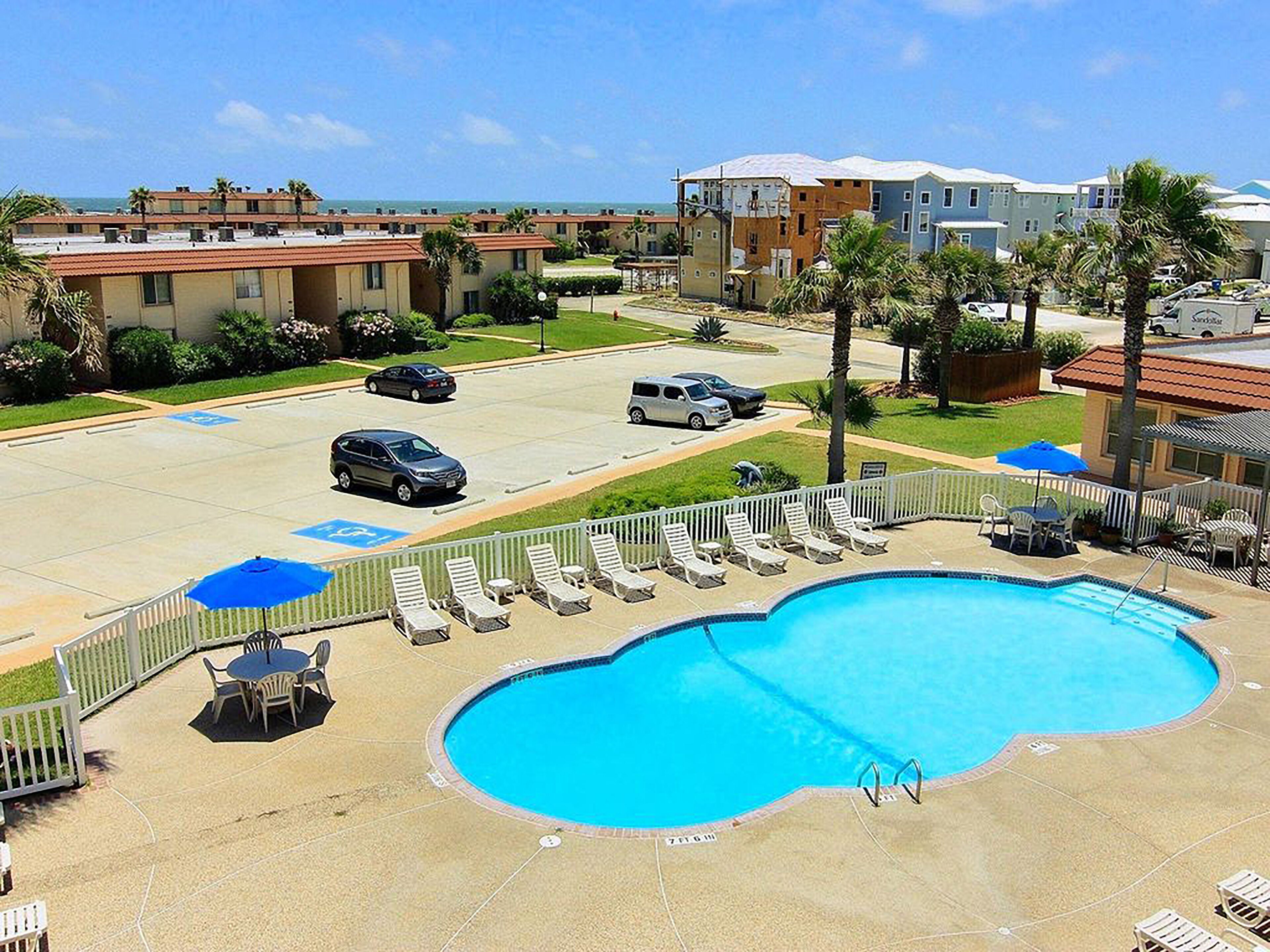 A hotel with a swimming pool, lounge chairs, and a parking lot.