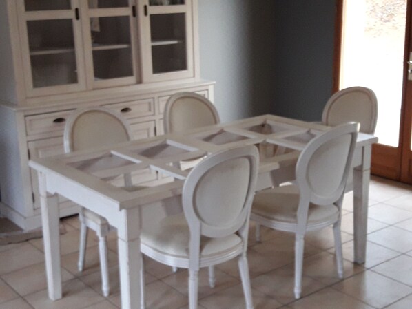A dining area with a white table and chairs, a cabinet with glass doors, and a tiled floor.
