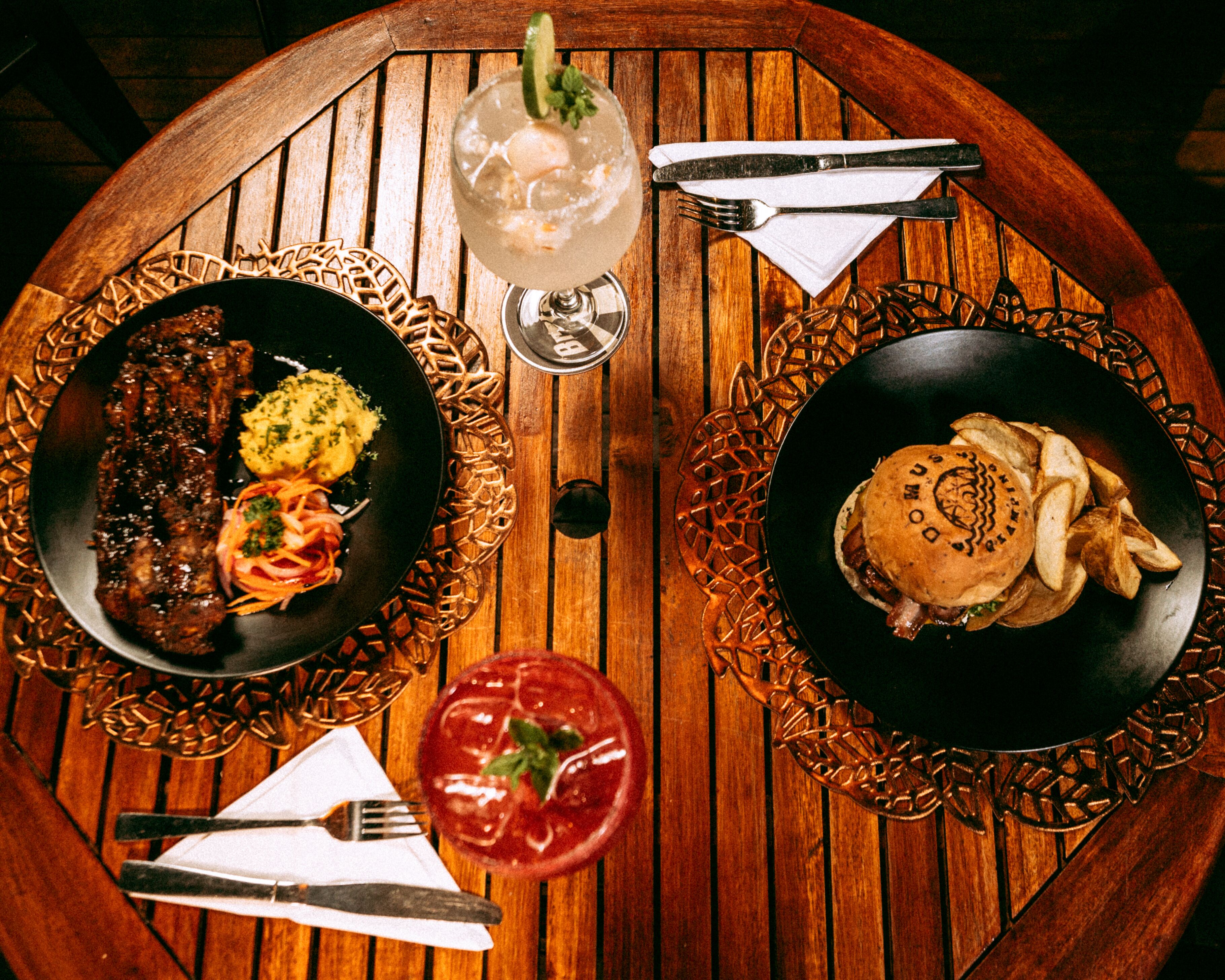 A wooden table with two plates of food, a glass of drink, and cutlery.