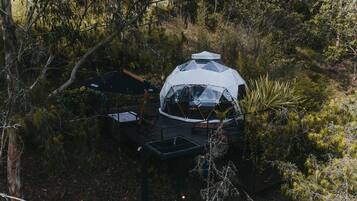En geodisk kupolkonstruktion med en terrass och ett avskärmat sittområde, omgiven av tät skog.