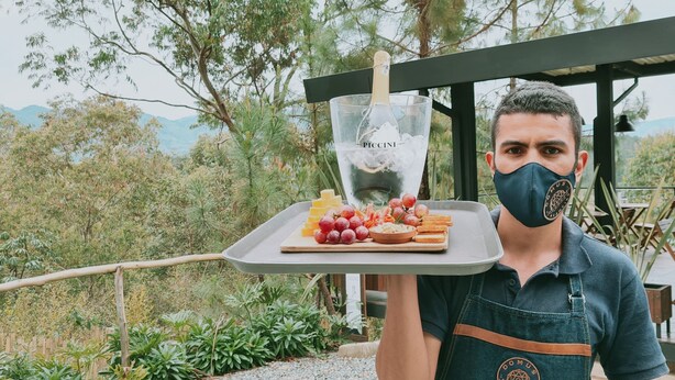 Eine Person hält ein Tablett mit einer Flasche PACCINI Champagner, Trauben und Käse.