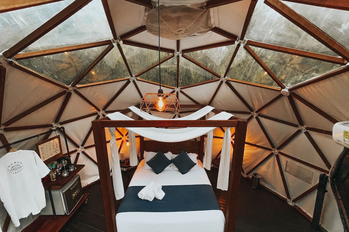 A cozy interior with a wooden bed, a hanging light fixture, and a view through a geometric window structure.