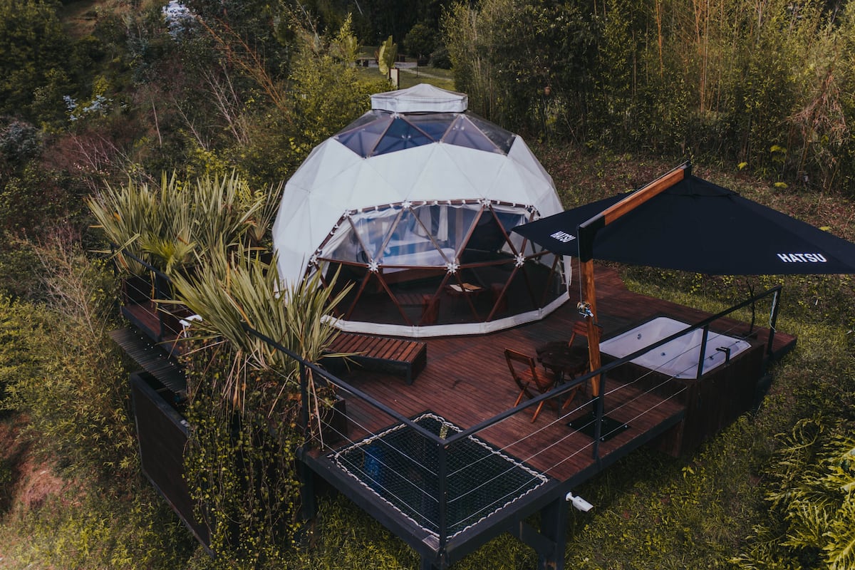 A geodesic dome structure with a wooden deck, outdoor seating, and a large umbrella.