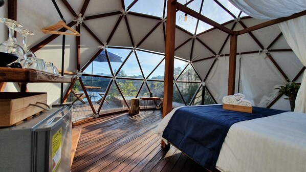 A tent-style room with a bed, wooden furniture, and a view of the outdoors.