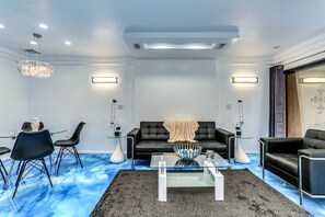 Een moderne woonkamer met een zwarte leren bank, een glazen salontafel en een eethoek met een glazen tafel en stoelen.