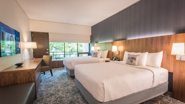 A hotel room with two beds, a desk, a chair, and a TV. - Inn at Villanova University (Wayne)