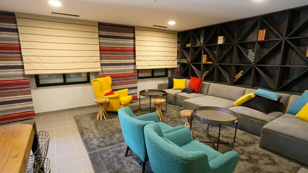 A modern living room with a sectional sofa, teal armchairs, a coffee table, and a bookshelf. - Hi Setubal Pousada de Juventude - Hostel (Setubal)