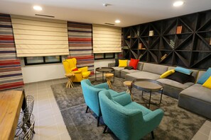 A modern living room with a sectional sofa, teal armchairs, a coffee table, and a bookshelf. - Hi Setubal Pousada de Juventude - Hostel (Setubal)