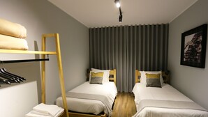 A hotel room with two single beds, a wooden ladder, a shelf with towels, a framed picture on the wall, and a window with curtains. - Hi Setubal Pousada de Juventude - Hostel (Setubal)