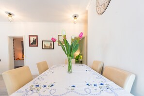 Ruokailutila, jossa on neljälle katettu pöytä, sen ympärillä tuoleja ja pöydän keskellä maljakko, jossa on kukkia.