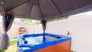 Ein Whirlpool unter einer Markise, im Hintergrund eine Ziegelwand und ein Grill.