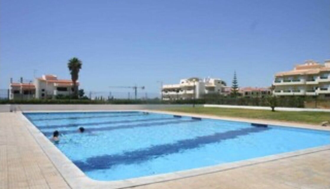 A swimming pool with two people in the water, surrounded by buildings.