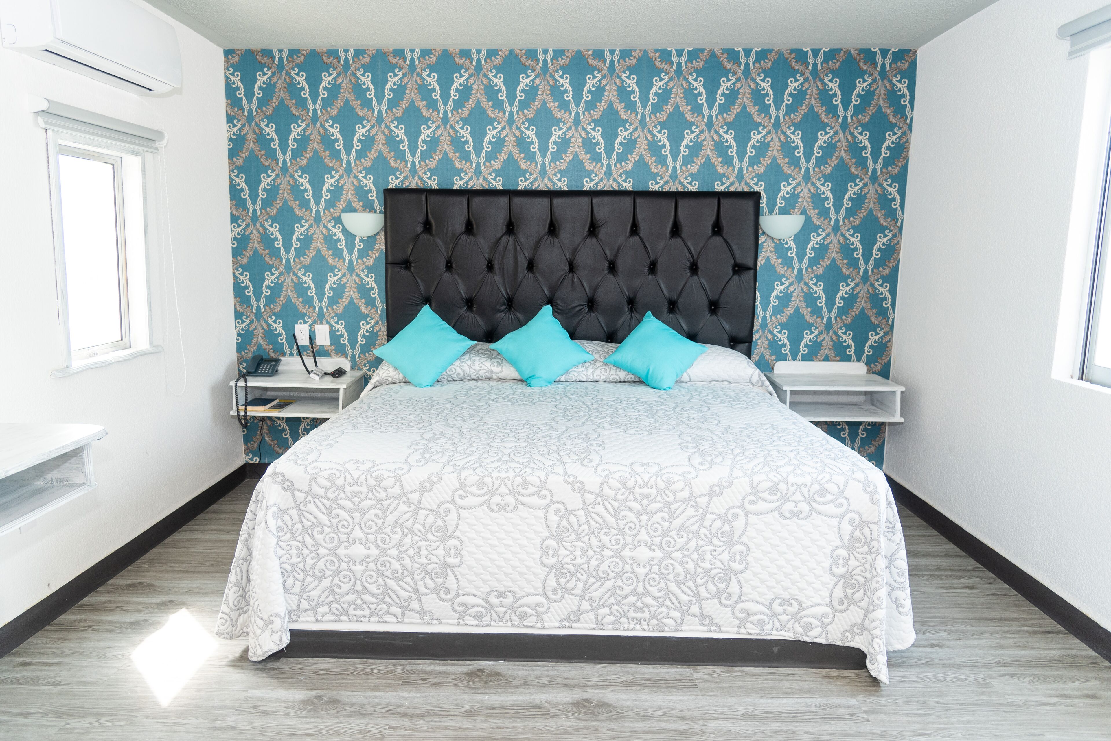 A modern bedroom with a tufted headboard, a patterned bedspread, and two matching pillows.