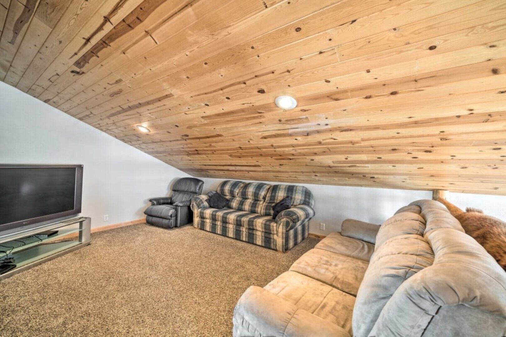Un salon chaleureux avec un plafond en bois, un téléviseur à écran plat, un canapé en cuir, un canapé à motifs et un grand fauteuil.
