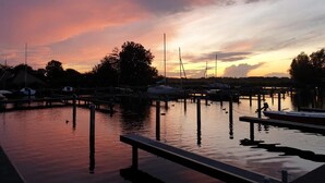 Un port de plaisance avec des bateaux amarrés à des quais en bois, une eau calme et un ciel au coucher du soleil.