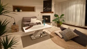 Un salon chaleureux avec un canapé, une table basse et une cheminée. On y trouve des plantes et une étagère murale décorative.