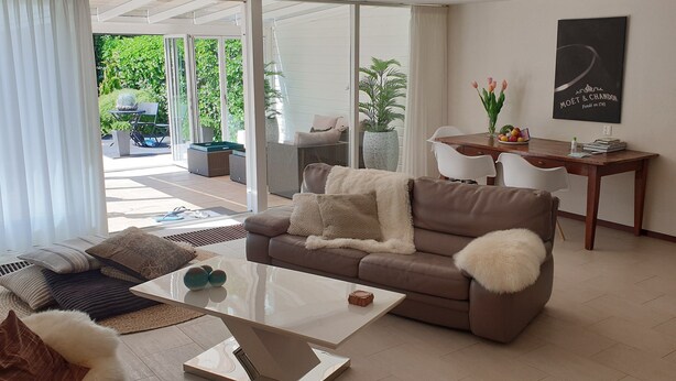 Un salon moderne avec un canapé marron, une table basse en verre et un coin repas comprenant une table et des chaises en bois.