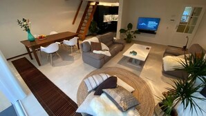 Un salon moderne comprenant un coin repas, un ensemble de canapés, une table basse et un téléviseur fixé au mur.
