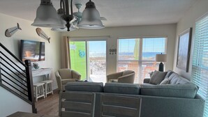 Un salon comprenant un canapé d’angle, une table basse avec un plateau sur lequel sont pliés des serviettes, un téléviseur et un escalier doté d’une rampe.