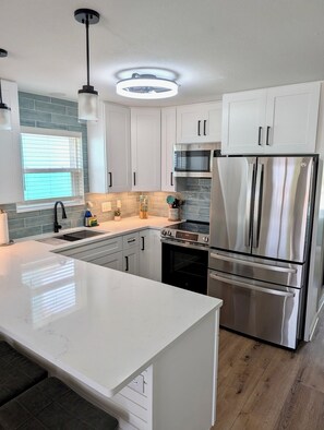 Una cocina moderna con armarios blancos, electrodomésticos de acero inoxidable, una isla grande y un ventanal con persianas.