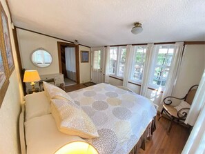 A bedroom with a large bed, a bedside table with a lamp, a chair, and a window with curtains.