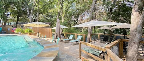 Un espace piscine doté d’une terrasse en pierre, de chaises longues et de parasols.