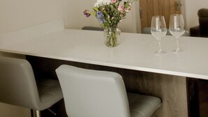 Een moderne eethoek met een witte tafel, grijze stoelen, hangende hanglampen en een vaas met bloemen.
