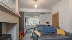 Een moderne woonkamer met een open haard, een leren bank en een eethoek op de achtergrond.