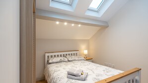 Een slaapkamer met een bed, een nachtkastje, een lamp en een dakraam.