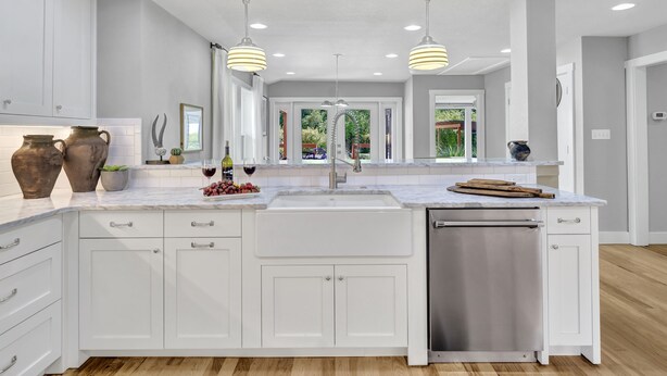 Una cocina moderna con armarios blancos, lavavajillas de acero inoxidable e iluminación colgante.