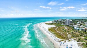 A coastal beach with a clear view of the ocean, a sandy shoreline, and a residential area with buildings. - Blu Sky Cottage | Waterfront Pool Home, Resort-Style Backyard, Near Siesta Key Village (Siesta Key)