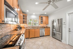 A kitchen with wooden cabinets, a stainless steel refrigerator, a microwave, and a dishwasher. - Blu Sky Cottage | Waterfront Pool Home, Resort-Style Backyard, Near Siesta Key Village (Siesta Key)