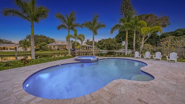 Piscina com hidromassagem, rodeada por palmeiras e vista para um lago.
