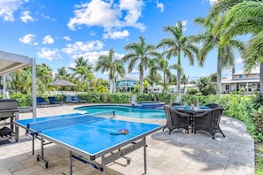 Un área de piscina con mesa de ping pong, sillas de descanso y una zona de estar cubierta.
