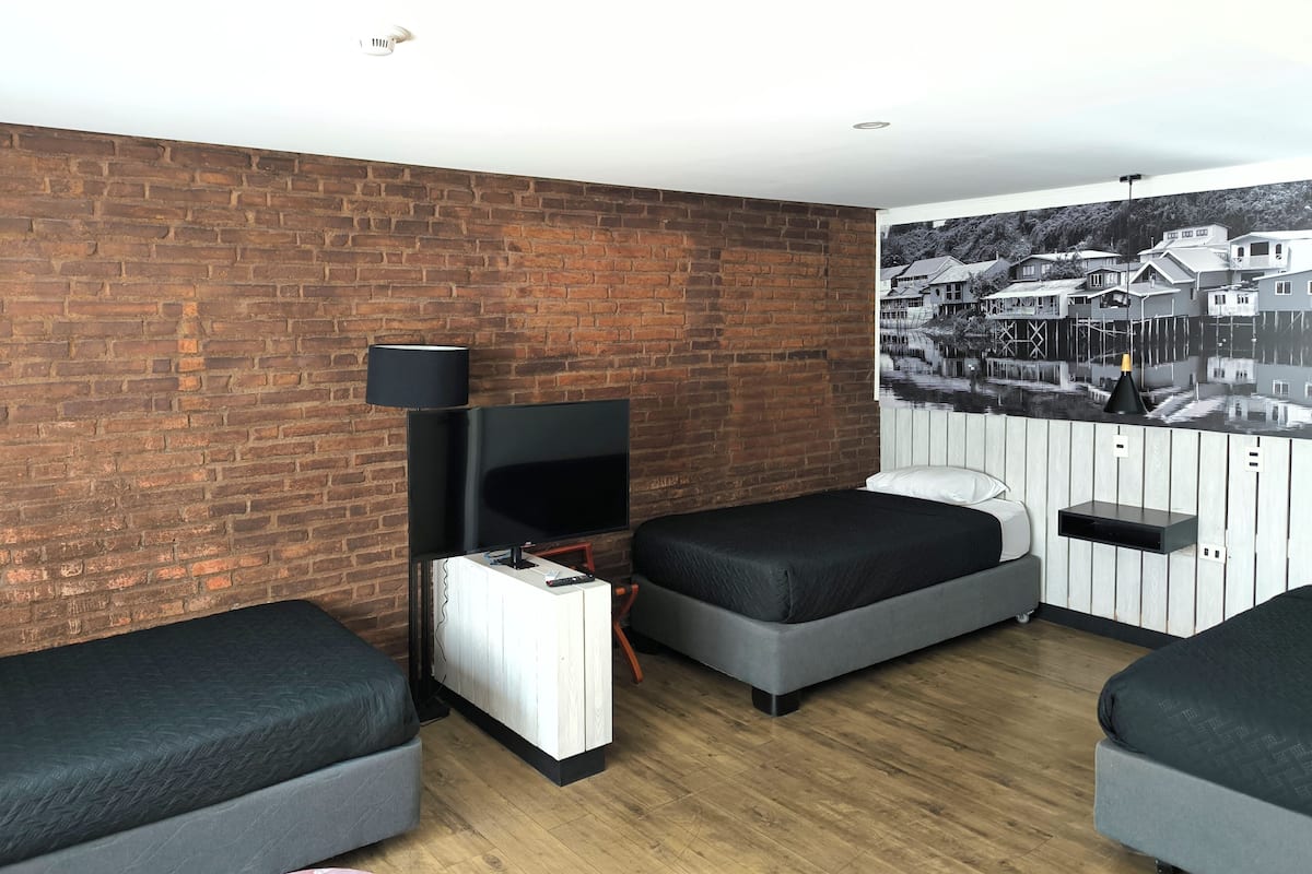 A room with a brick wall, a flat-screen TV, two grey sofas, a white cabinet, and a black lamp.