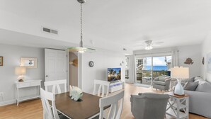 A modern living room with a dining area, a grey armchair, a white sofa, and a view of the ocean through large windows. - A Slice Of Paradise! Beautiful Ocean Views And Just Steps From The Beach (Panama City Beach)