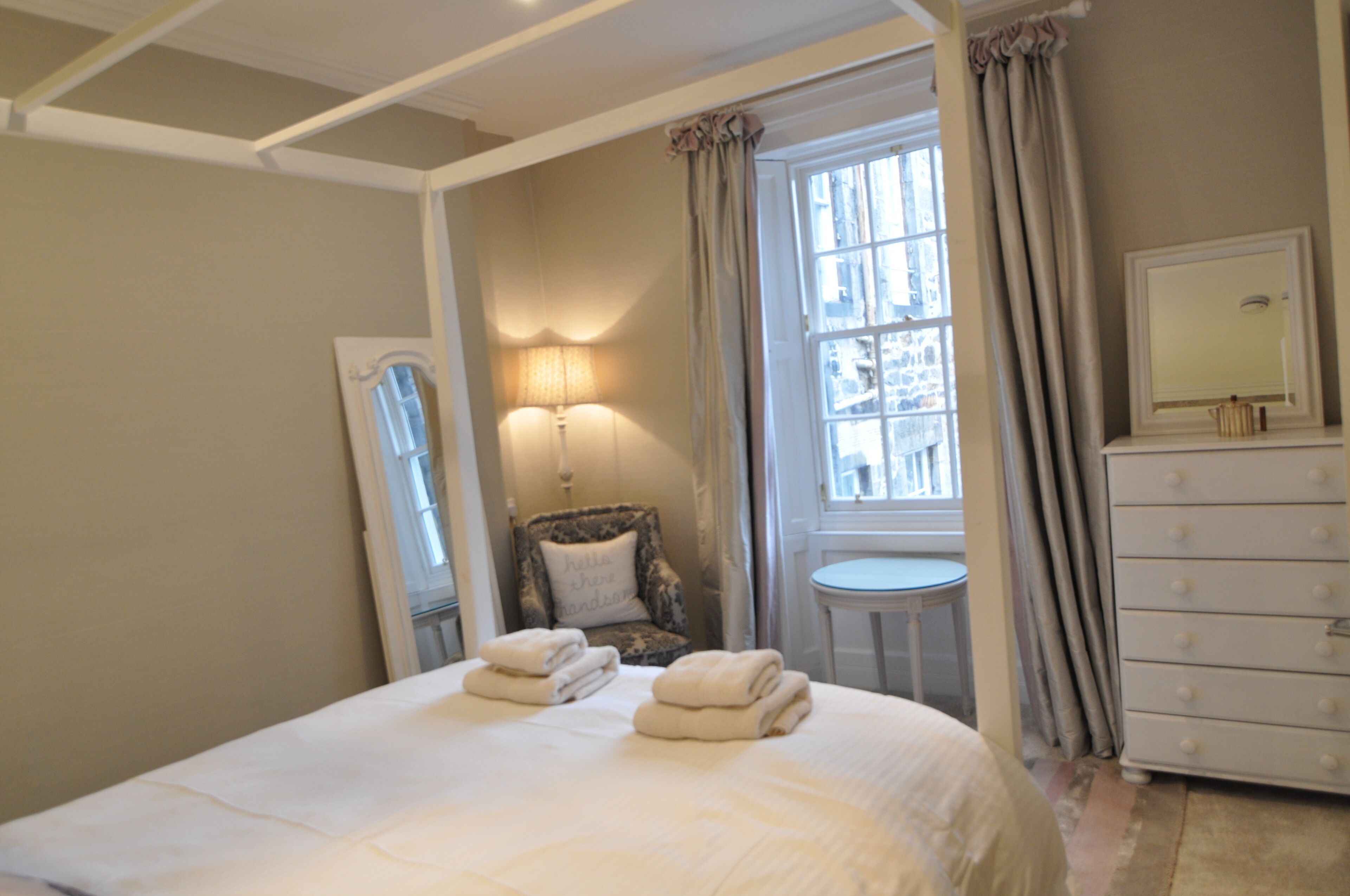 A bedroom with a bed, a chair, a dresser, a lamp, and a window.