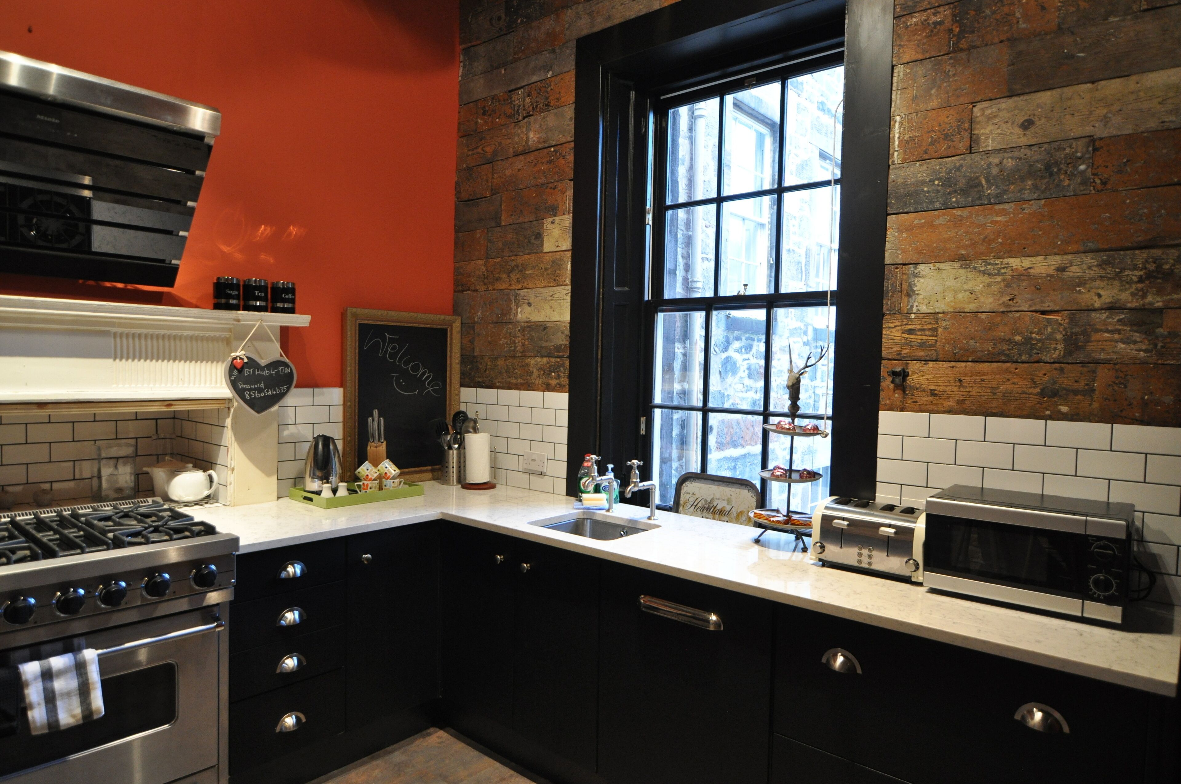 A kitchen with a gas stove, microwave, and toaster. There is a window with a view of trees and a brick wall.