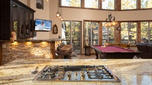 A kitchen with a gas stove, a pool table, and a bar area with stools.