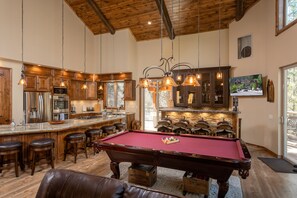 Un vaste espace de vie comprenant une table de billard, un bar en bois et une grande cuisine équipée d’appareils électroménagers modernes.