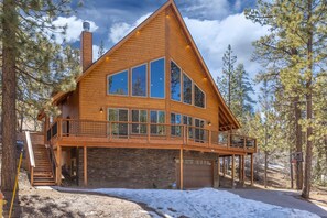 Une cabane en bois dotée d’un balcon, de grandes fenêtres et de fondations en pierre.