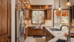 A modern kitchen with wooden cabinets, stainless steel appliances, a large island with a sink, and pendant lighting.