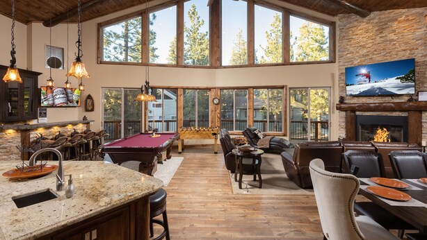 A spacious living area with a pool table, comfortable seating, a fireplace, and large windows offering a view of the outdoors.
