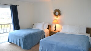 A hotel room with two beds, a window with a curtain, a nightstand with a lamp, and a wall-mounted wreath. - Two separate Apartments (Wachapreague)