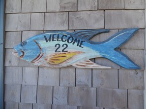 Un panneau en bois en forme de poisson, sur lequel on peut lire le texte « BIENVENUE 22 », est fixé à un mur en bois.