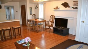 A living room with a wooden floor, a dining table with chairs, a TV, and a fireplace. - Two separate Apartments (Wachapreague)