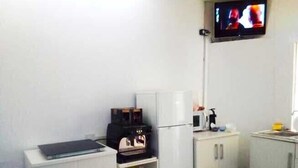Eine kleine, kompakte Küche mit weißen Schränken, einer Mikrowelle, einer Kaffeemaschine und einem an der Wand befestigten Fernseher.
